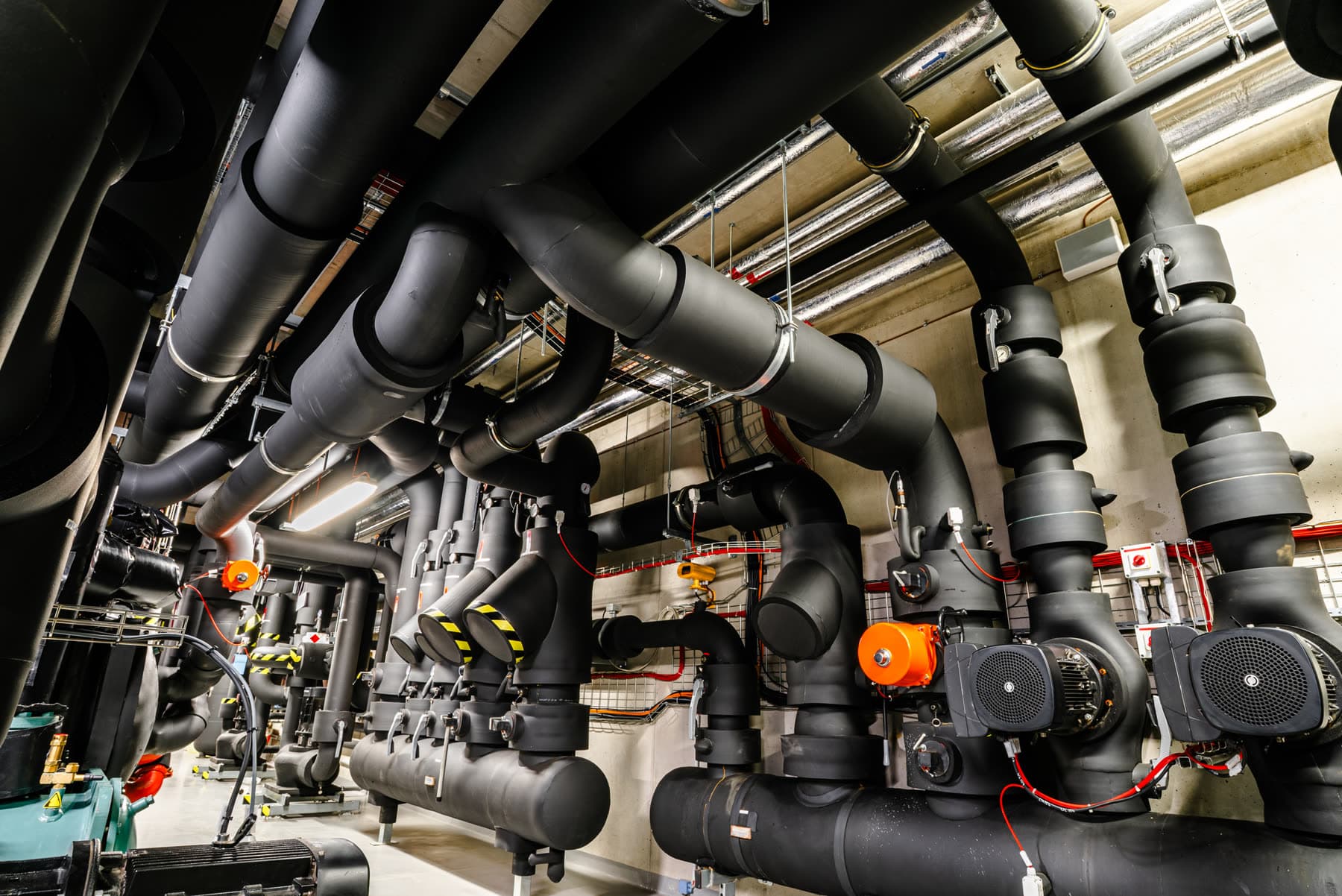 Black-insulated industrial HVAC piping and pumps in a mechanical room